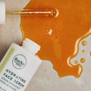 A bottle of Essential Face Cream & Hydrating Natural Face Serum with its dropper resting in a pool of amber liquid.